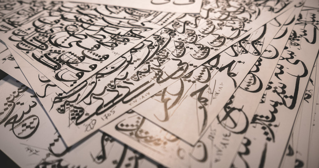 Stack of papers full of Arabic calligraphy training drills in Thuluth script, done in black sumi ink.