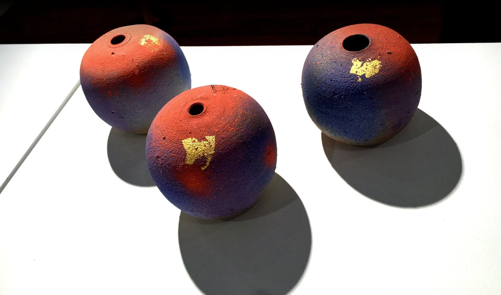 Three colorful ceramic spheres with red, blue, and gold accents on a white background.