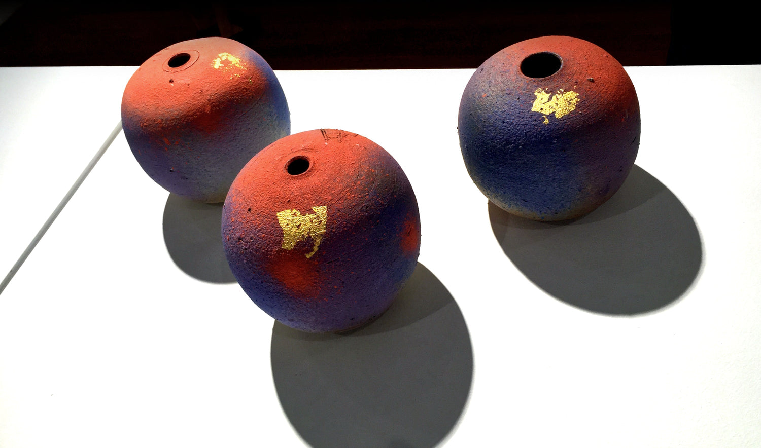 Three colorful ceramic spheres with red, blue, and gold accents on a white background.
