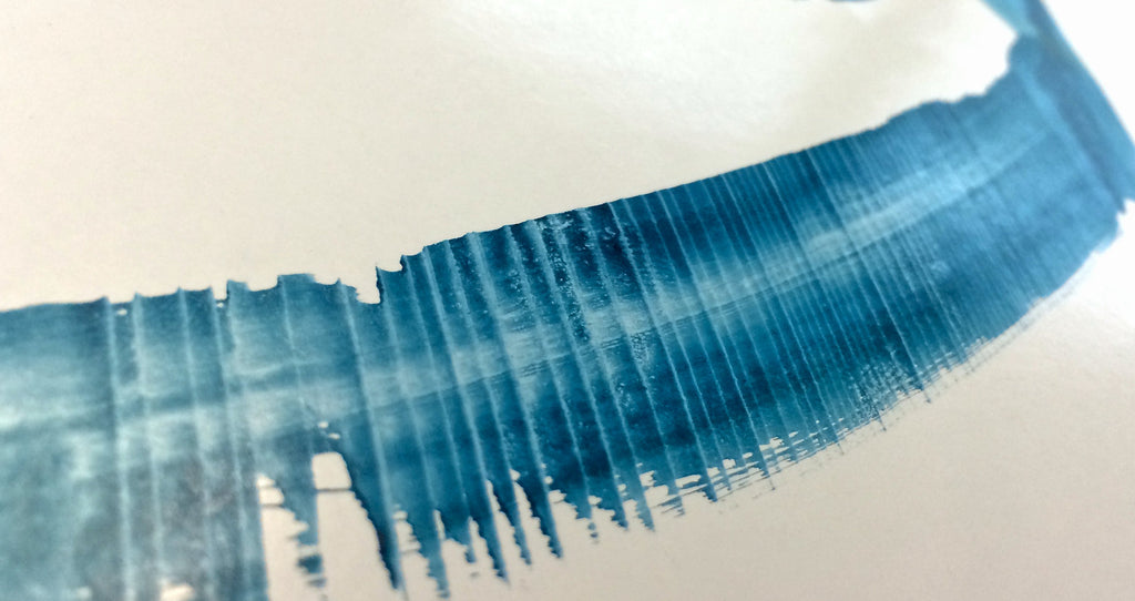 A close up detail view of a stroke of ink movement made by a traditional wooden calligraphy pen using a blue turquoise ink on semi-gloss art paper.