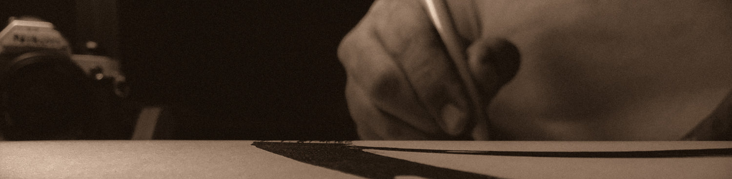 Artist holding calligraphy pen on a piece of work.