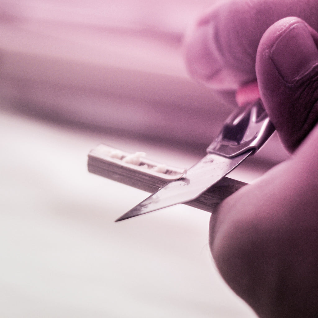 Hand holding a penknife carving bamboo wood to make a traditional calligraphy pen.